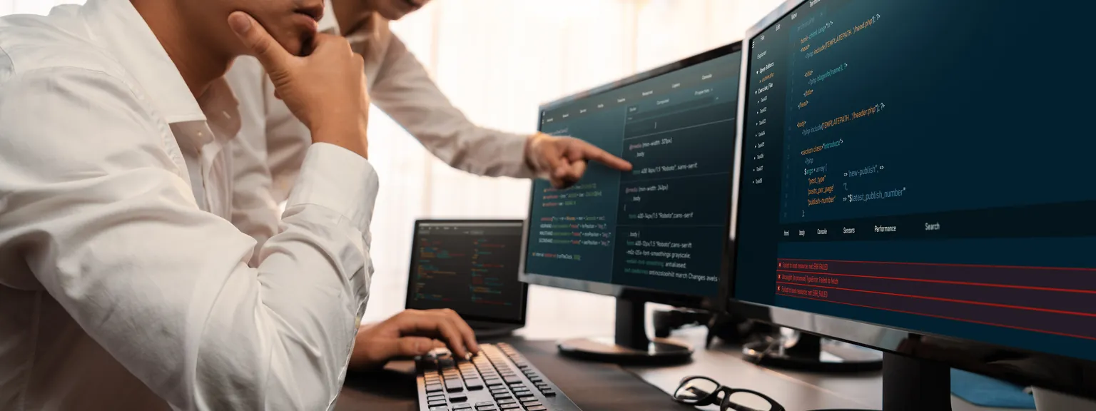 Engineers reviewing source code together across large monitors